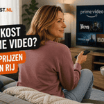 Sanne zit zijwaarts op een bank met een afstandsbediening in de hand, gericht naar een televisie met Prime Video. Links staat de titel ‘Wat kost Prime Video?’ in zwarte en oranje tekstvlakken.